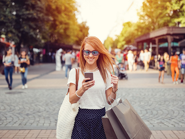 A women standing with shopping bags smiling at her phone