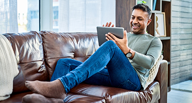 A guy sitting on a couch smiling on his tablet