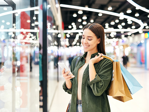 Women looking at her phone holding bags smiling