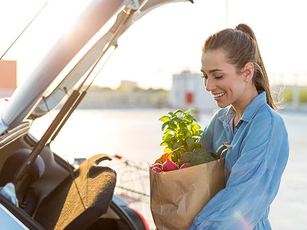 women holding a grocery bag smiling putting it into her car